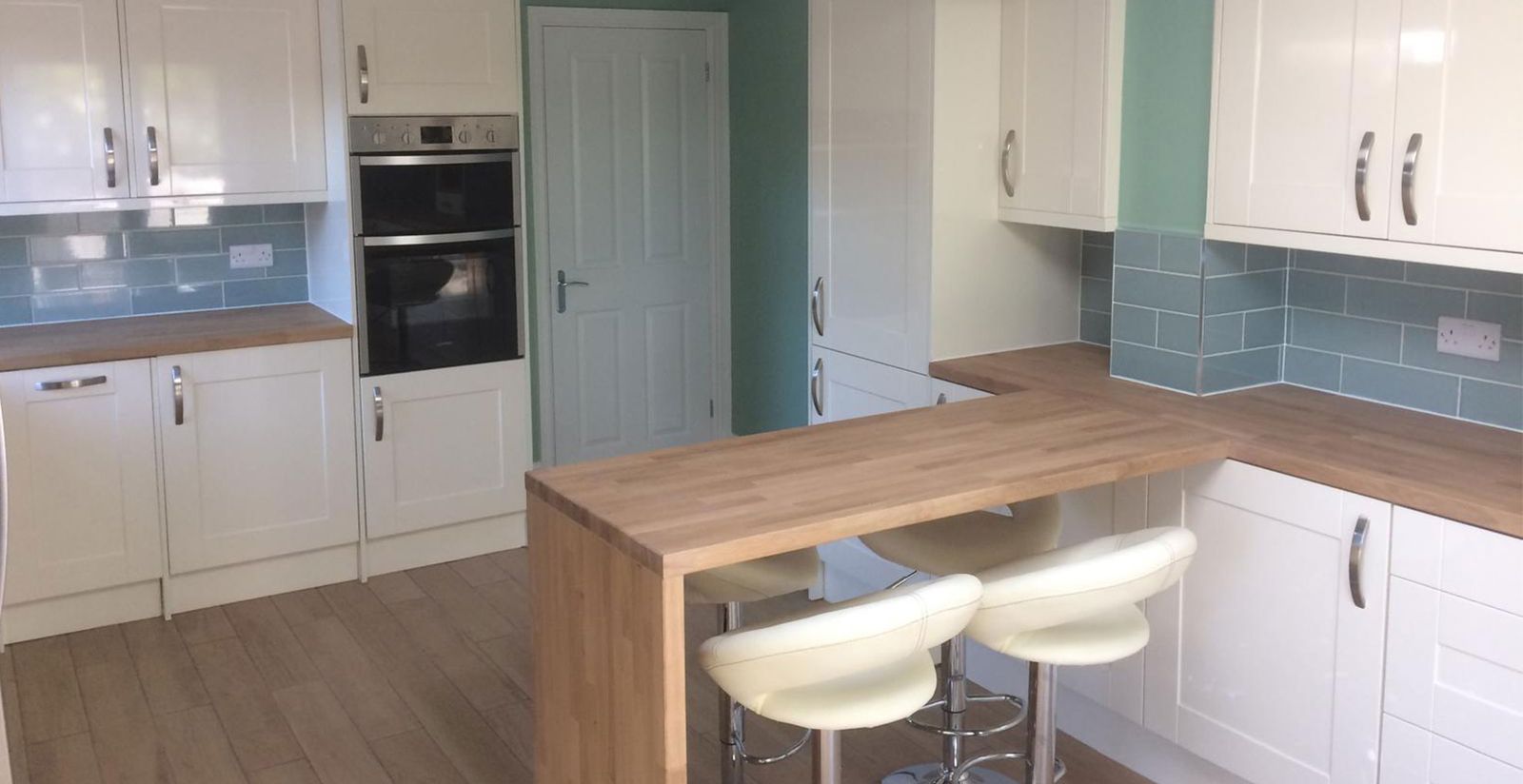 White shaker kitchen with a wood breakfast bar and sage green wall in a finished extension