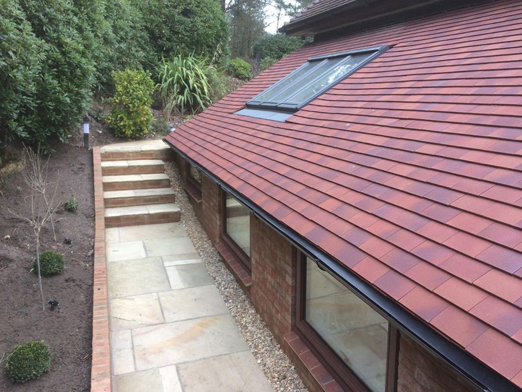 New clay tiled roof over a single storey extension with a sandstone patio and steps below