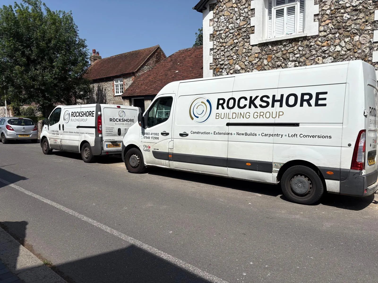 Two sign-written Rockshore Building Group vans parked beside a flint cottage